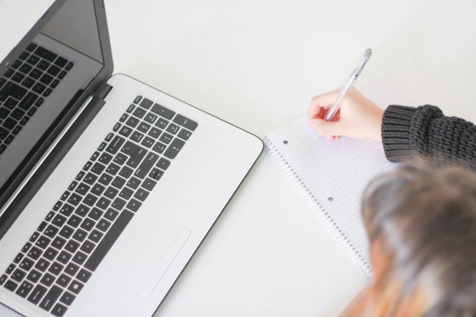 Free Image of Person Writing on Paper Next to Laptop 