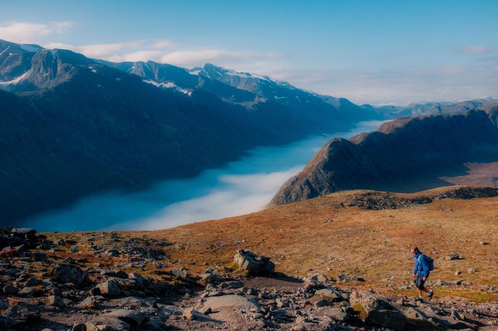 Free Image of Person Walking Up Hill With Mountains in Background 