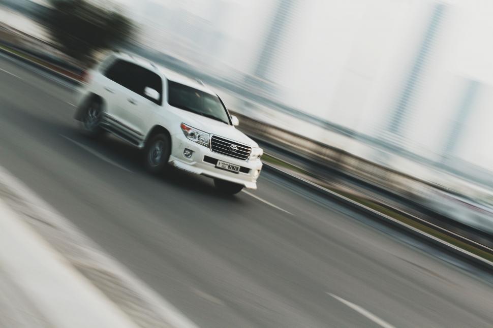 Free Image of White Van Driving Down Street Next to Tall Buildings 