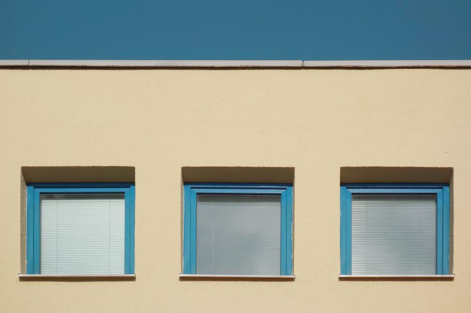 Free Image of Three Windows With Blue Trim on a Beige Building 
