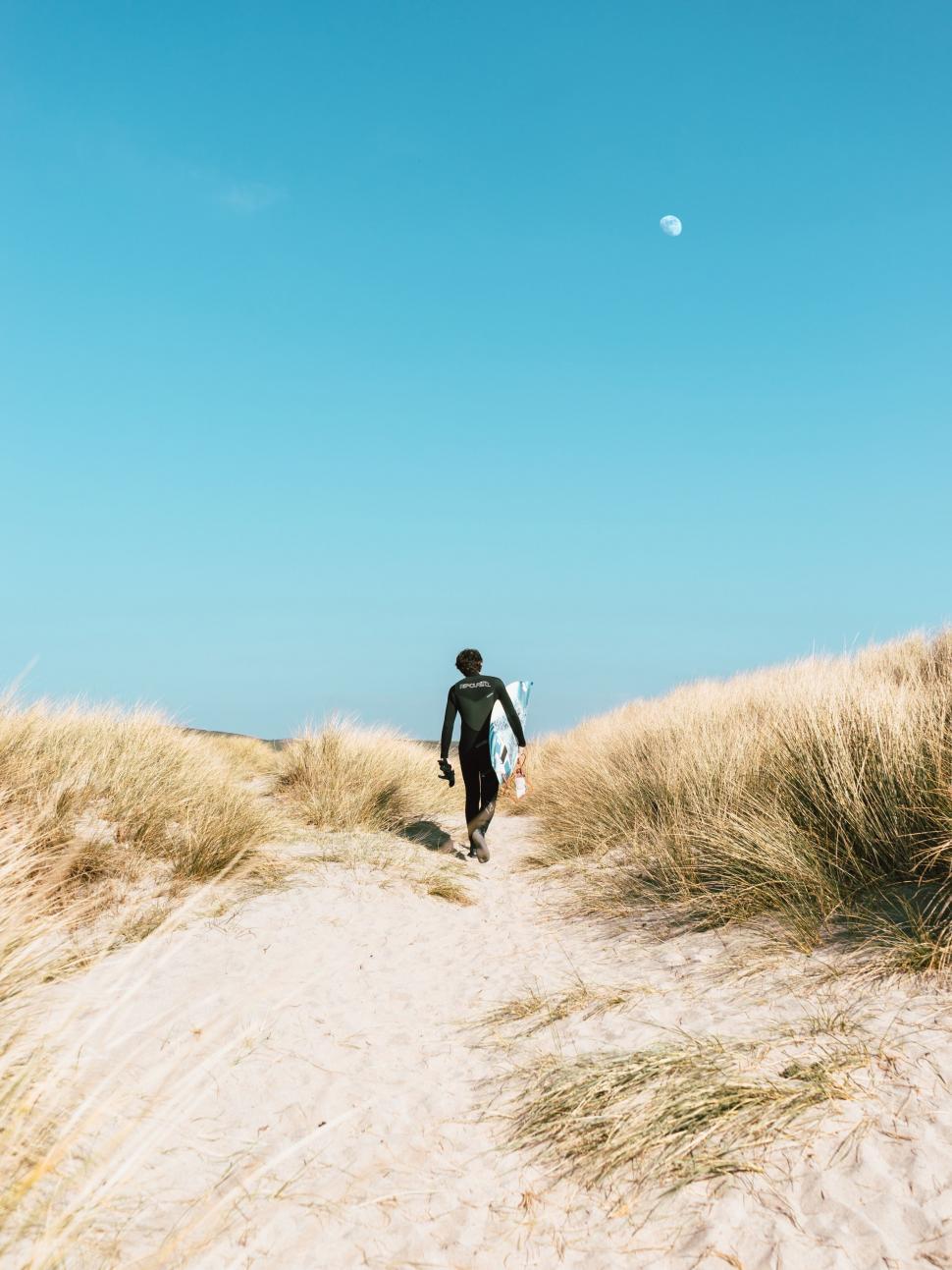 Free Image of Man Walking Up Sand Dune Towards Ocean 