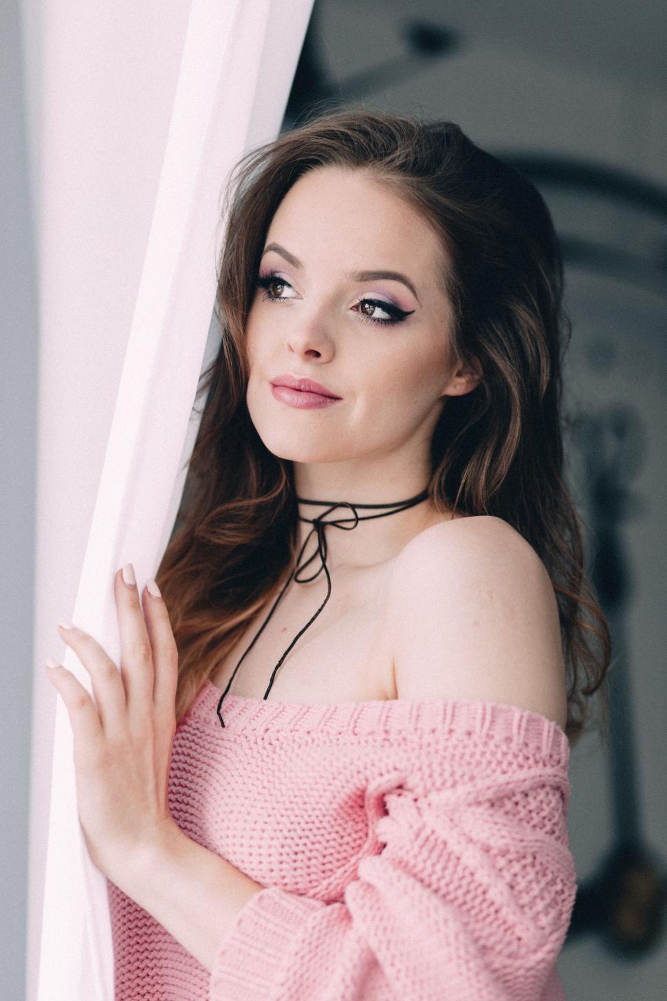 Free Image of Woman Wearing Pink Sweater Leaning Against Curtain 