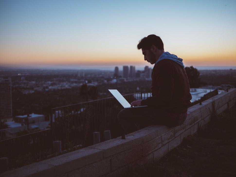 Free Image of Man Sitting on Ledge Using Laptop Computer 