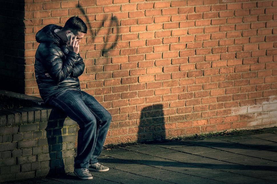 Free Image of Man Sitting on Brick Wall Talking on Cell Phone 