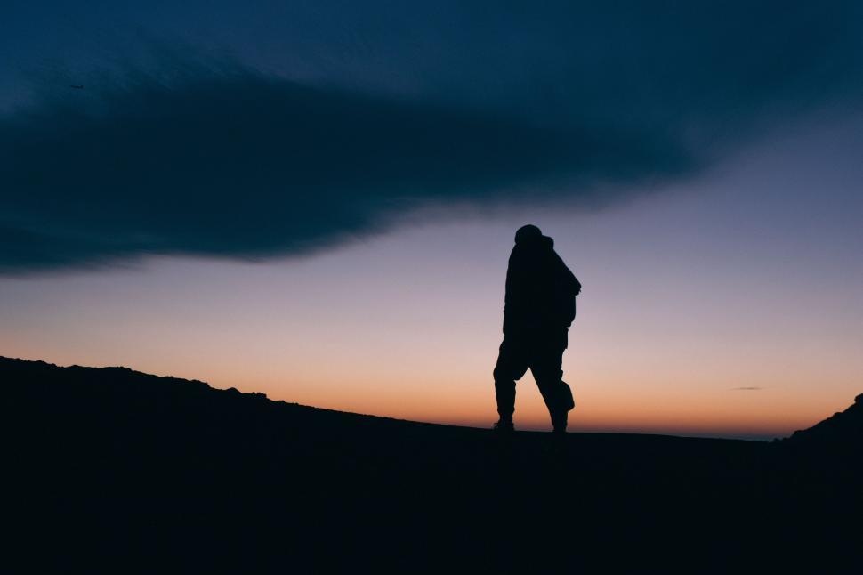 Free Image of Man Standing on Top of Hill Under Cloudy Sky 