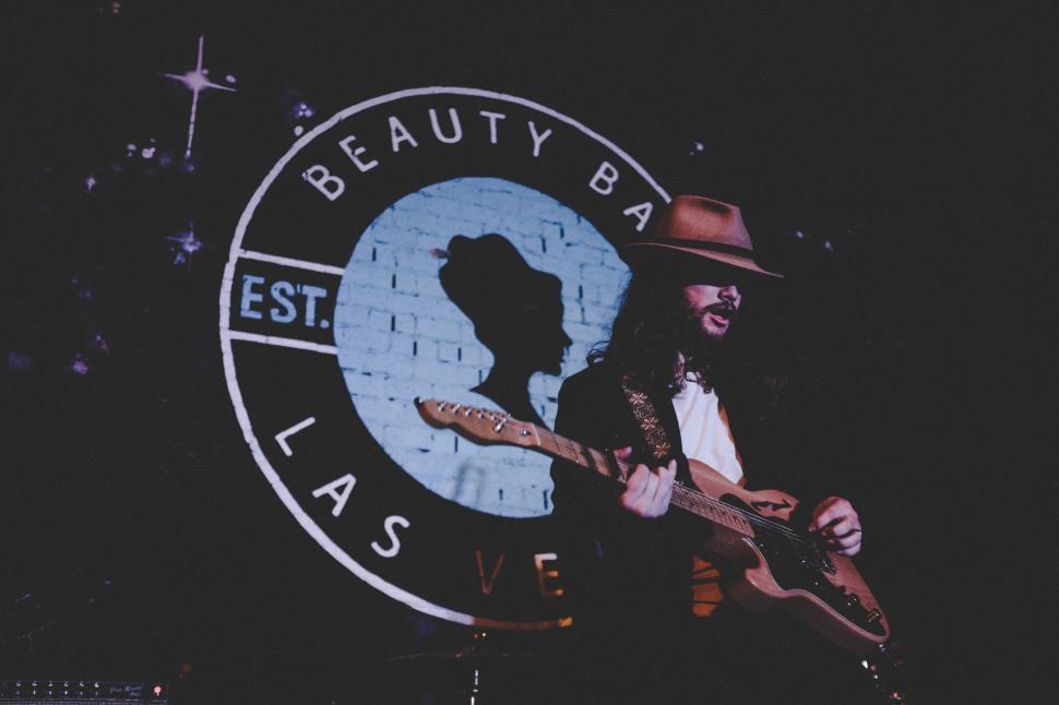 Free Image of Man Playing Guitar in Front of Sign 