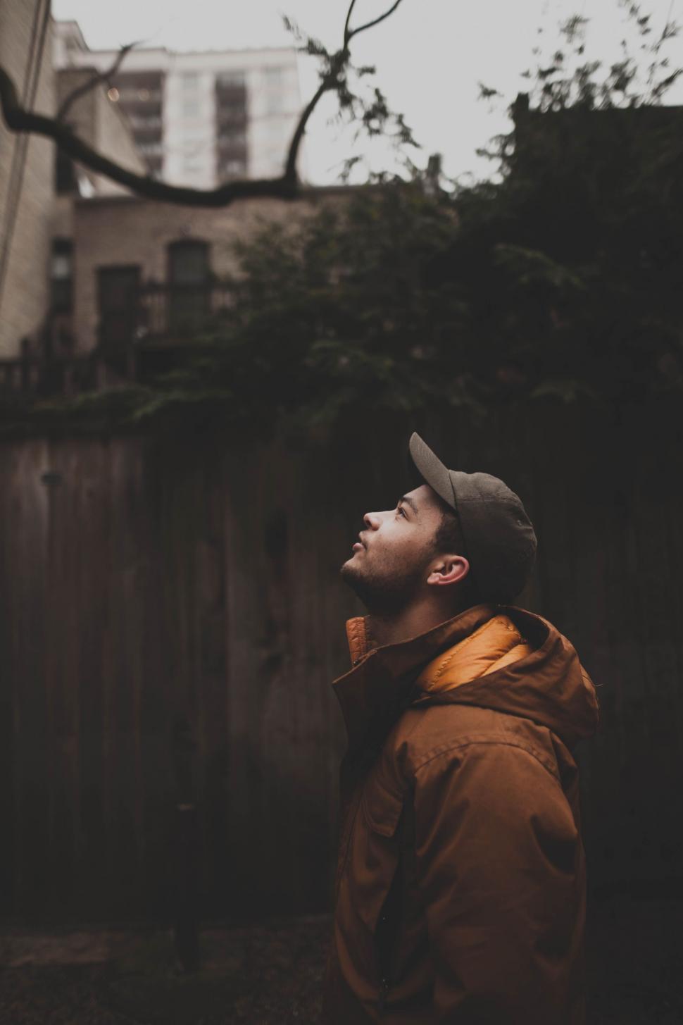 Free Image of Man in Hat and Jacket Standing in Front of Fence 