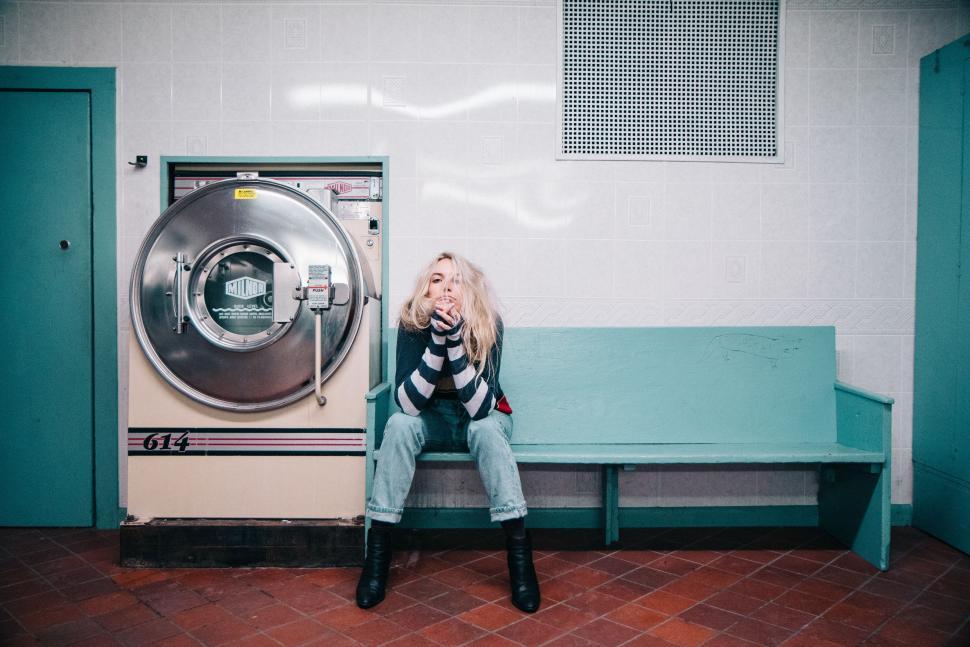 Free Image of Woman Sitting on Bench in Front of Washer 