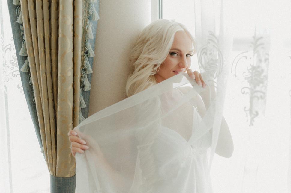 Free Image of Woman in White Dress Standing by Window 