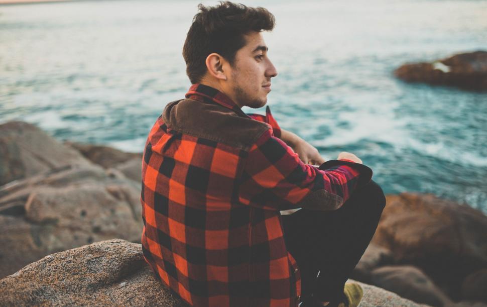 Free Image of Man Sitting on Top of Rock by Ocean 