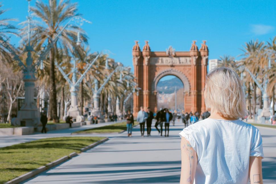 Free Image of Woman Walking Down Sidewalk With Palm Trees in Background 