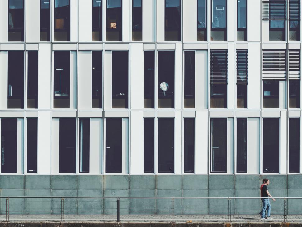Free Image of Man Walking Down Sidewalk Next to Tall Building 