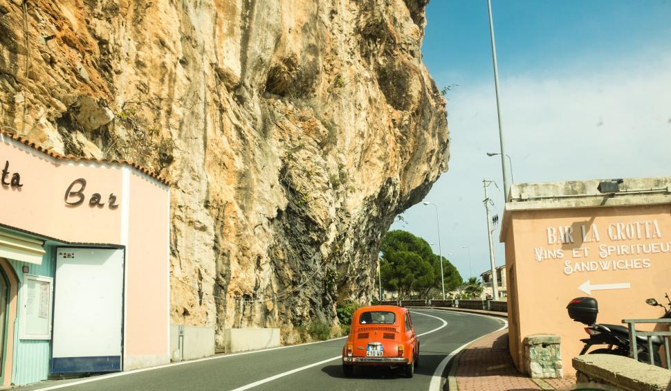 Free Image of Orange Car Driving Down Road Next to Cliff 