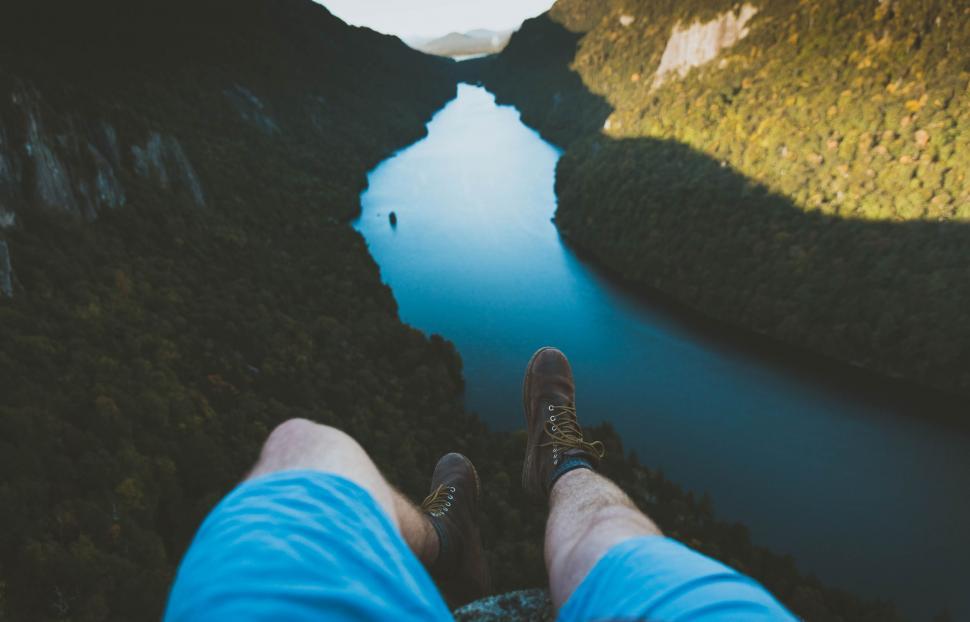 Free Image of Man Standing on Top of a Mountain Next to a River 