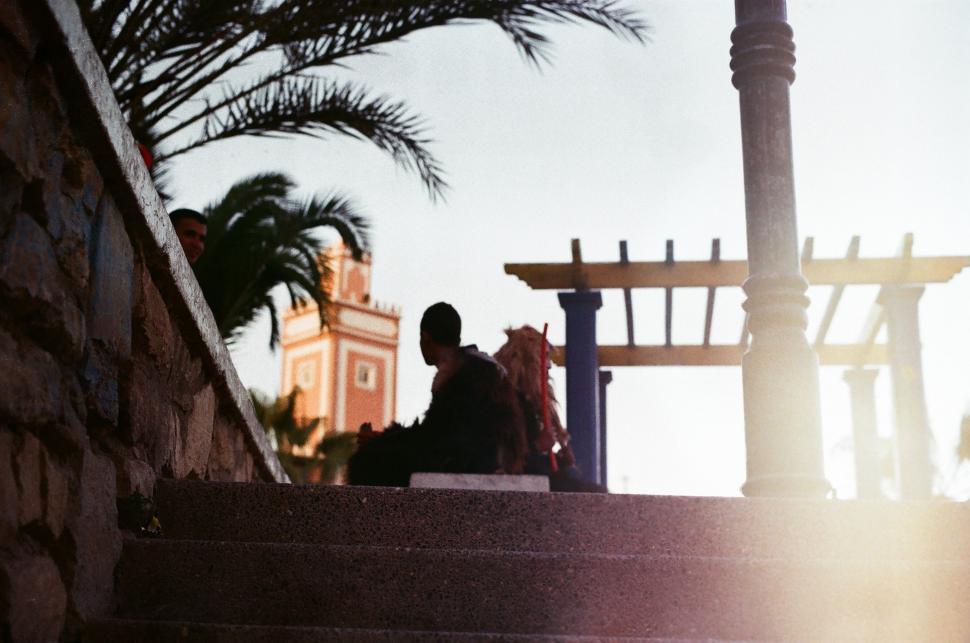 Free Image of Man Sitting on Stairs Next to Palm Tree 