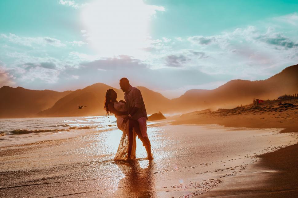 Free Image of Man and Woman Standing on Beach Next to Ocean 
