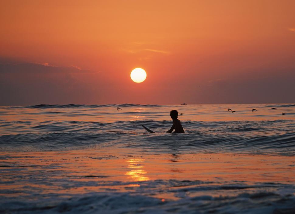 Free Stock Photo of Person Riding Surf Board in Ocean at Sunset