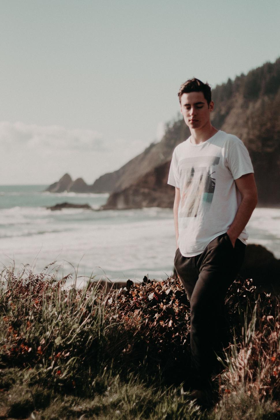 Free Image of Man Standing on Lush Green Hillside by Ocean 