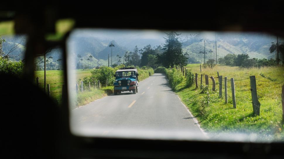 Free Image of Car Driving Along Road Next to Lush Green Field 