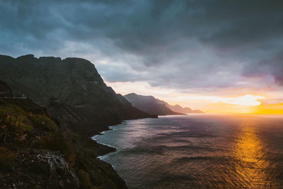Free Image of The Sun Sets Over the Ocean on a Cloudy Day 