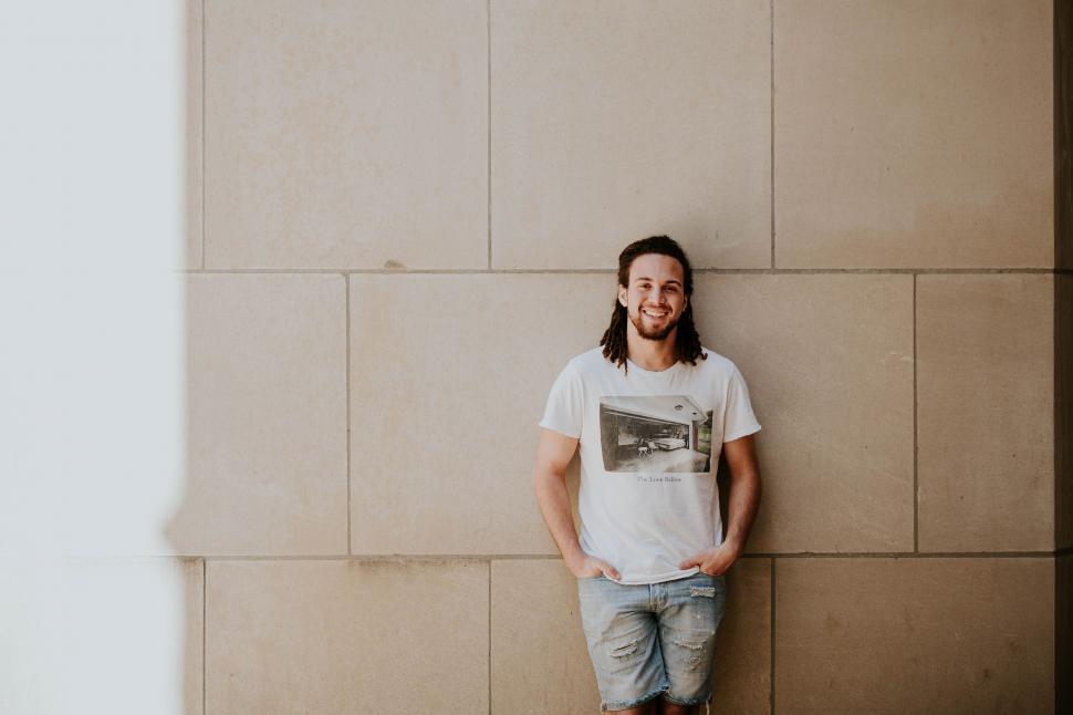 Free Image of Man Leaning Against Wall With Hands in Pockets 