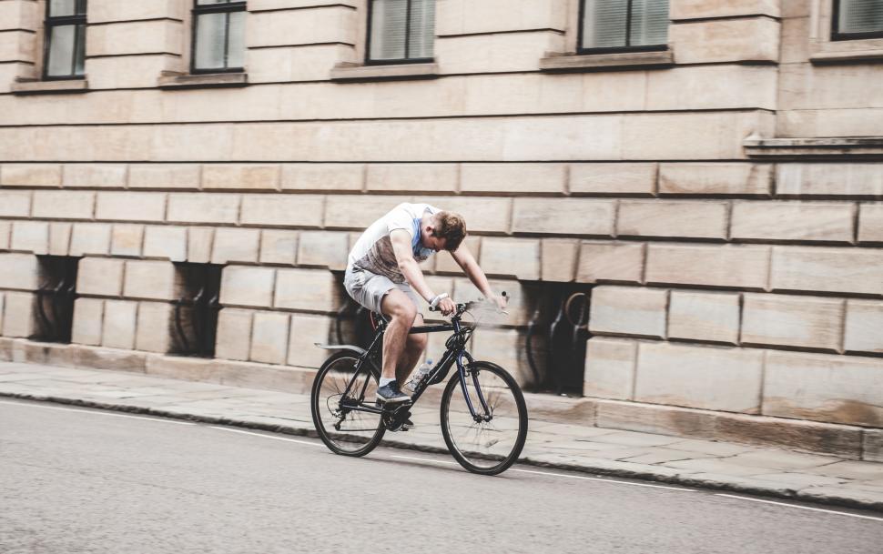 Free Image of Man Riding Bike Alongside Tall Building 
