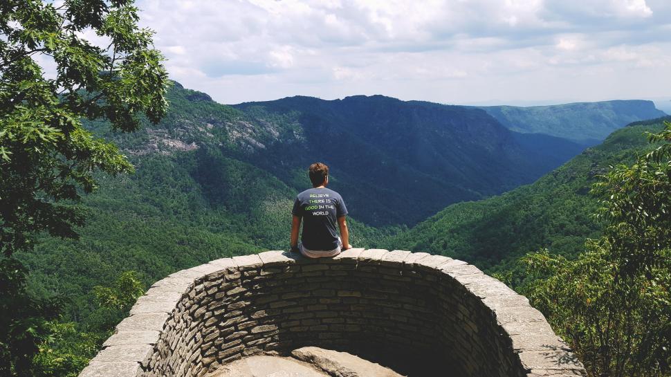 Free Image of Man Sitting on Top of Stone Wall 
