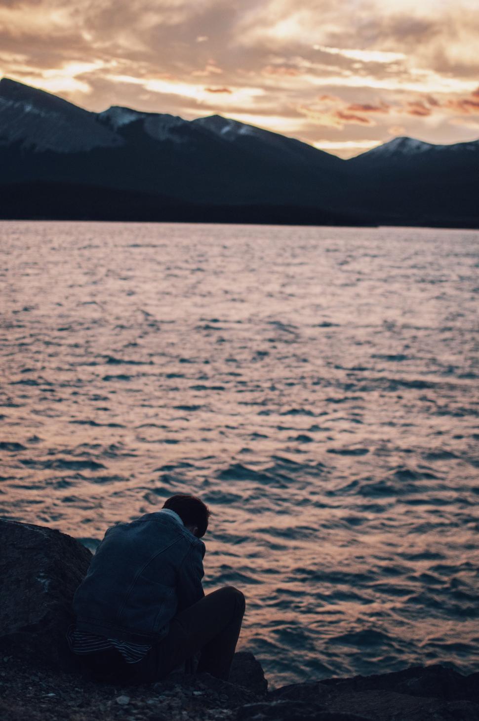 Free Image of Person Sitting on a Rock by Water 
