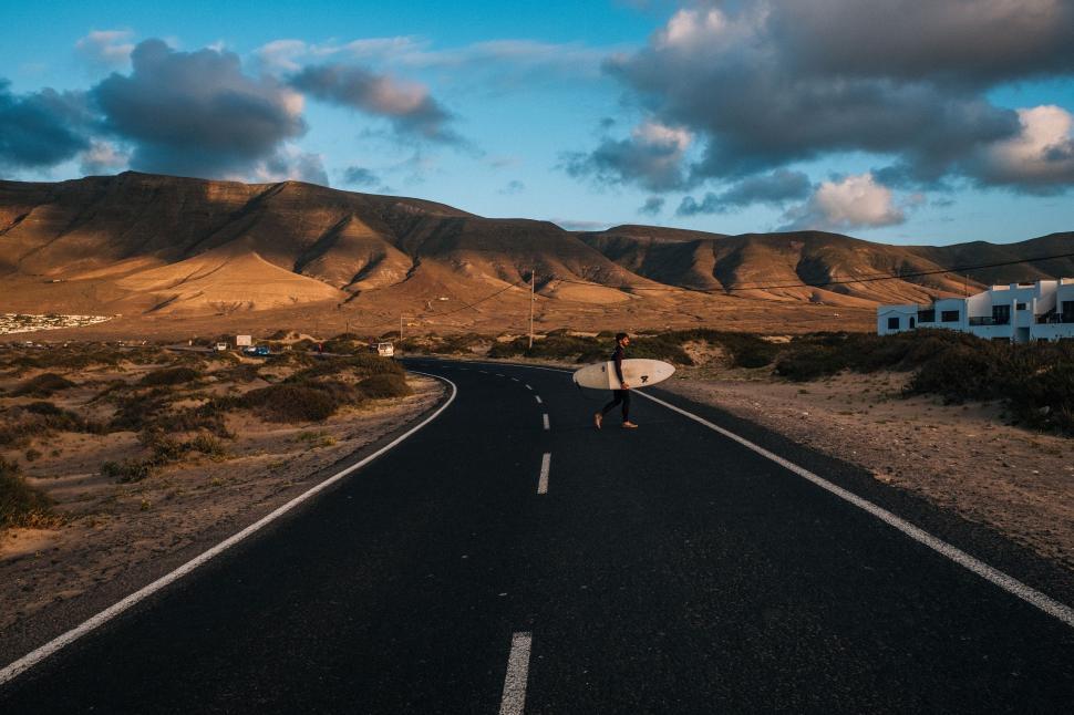 Free Image of Person Carrying Surfboard Across Desert Road 