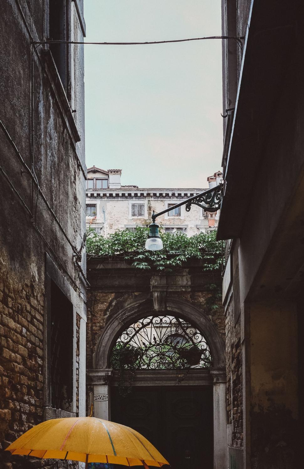 Free Image of Person Walking Down Alleyway With Yellow Umbrella 