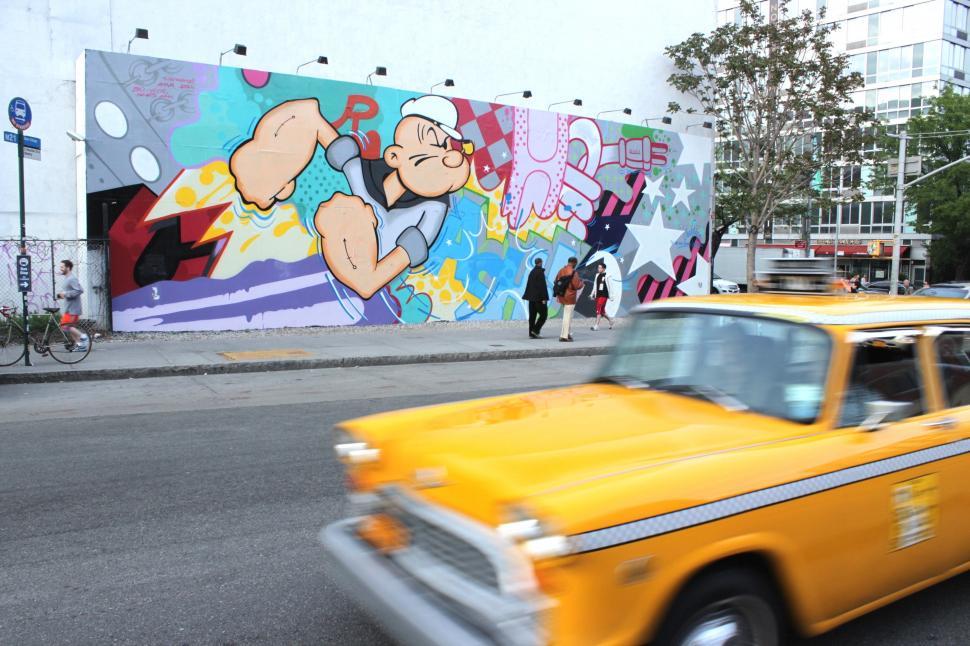 Free Image of Yellow Taxi Passing Graffiti Covered Wall 