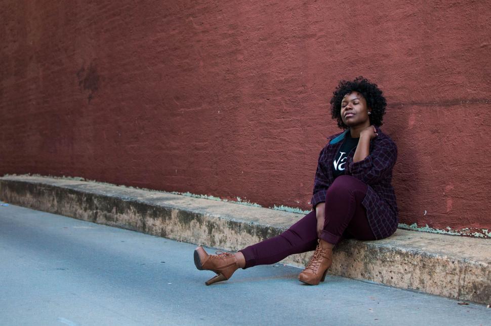 Free Image of Woman Sitting on Curb Next to Red Wall 