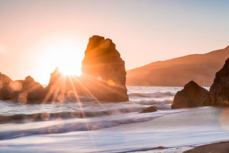 Free Image of Sun Setting Over Ocean With Rocks in Foreground 