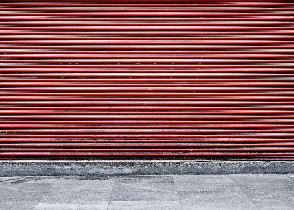 Free Image of Man Walking Down Sidewalk Next to Red Garage Door 