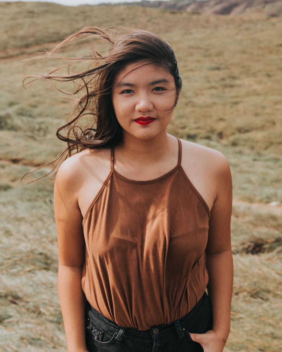 Free Image of Woman Stands in Field With Hair Blowing in Wind 