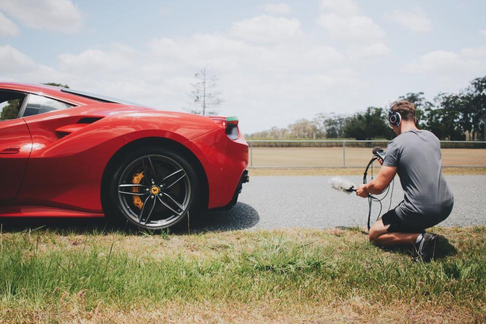 Free Image of Man Kneeling Next to Red Sports Car 