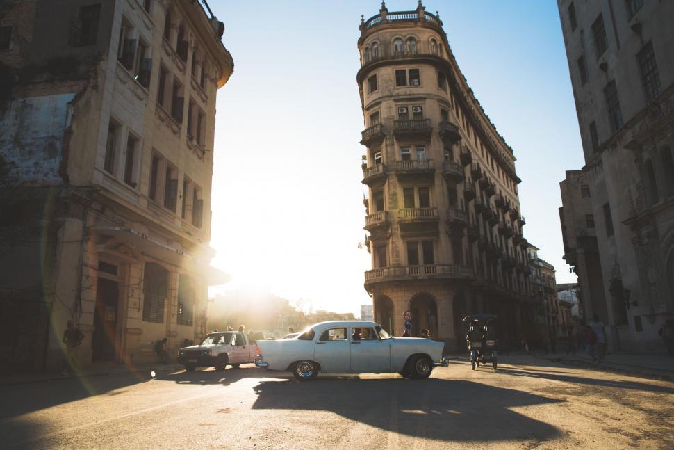 Free Image of White Car Driving Down Street Next to Tall Buildings 