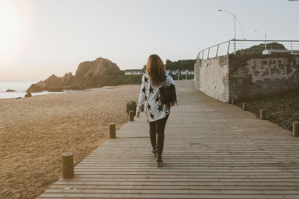 Free Image of Woman Walking Down Wooden Walkway Next to Ocean 