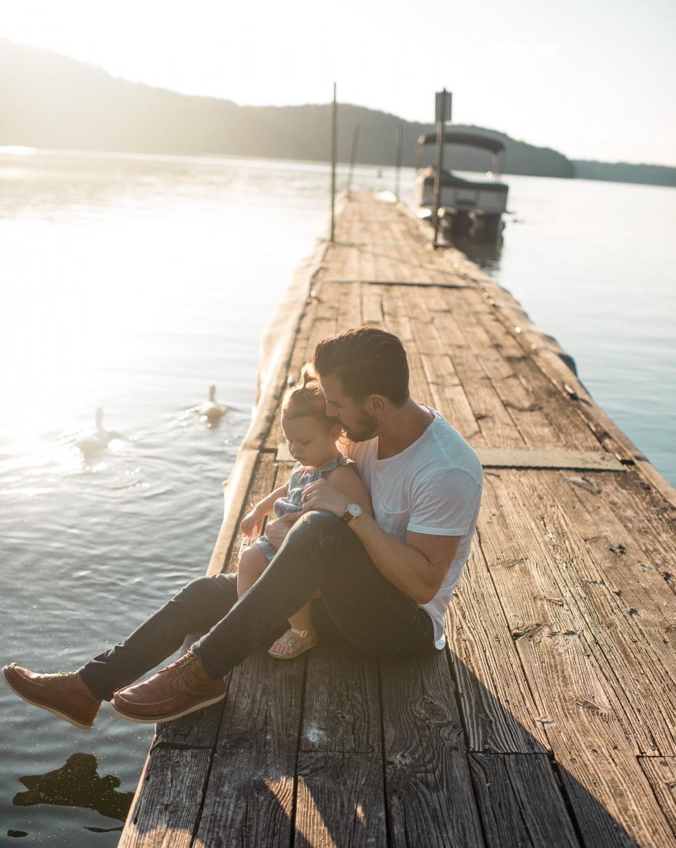 Free Image of Man Holding Baby Sitting on Pier 