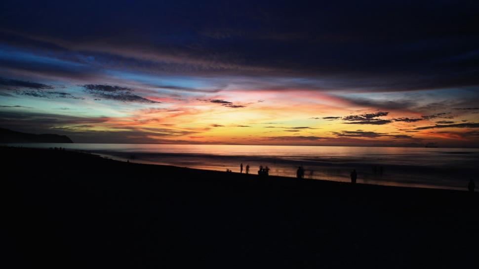 Free Image of Group of People Standing on Top of Beach Under Cloudy Sky 