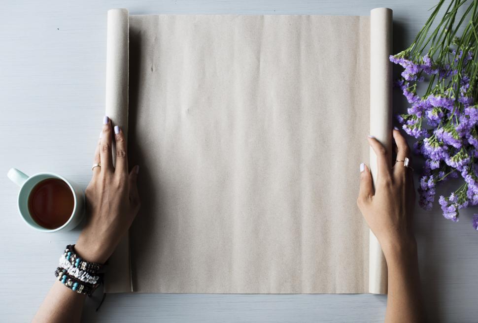 Free Image of Two Hands Holding a Roll of Paper Next to a Cup of Coffee 