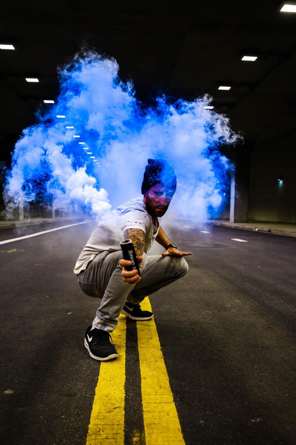 Free Image of Man Kneeling in Street With Blue Smoke 