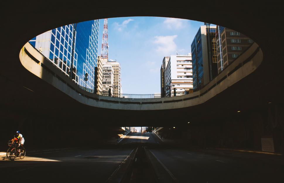 Free Image of Man Cycling Down Street Under Bridge 