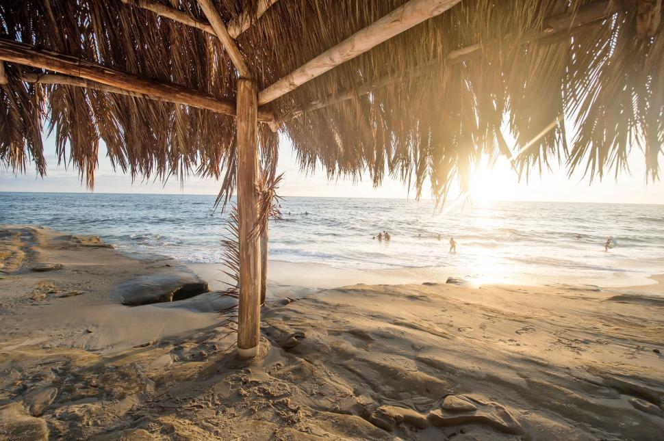 Free Image of Sun Shining Through Straw Umbrella on Beach 