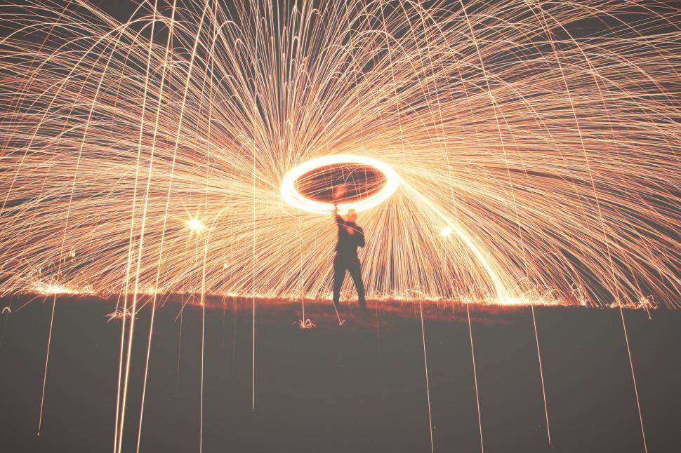 Free Image of Man Standing on Top of Hill Under Sky Filled With Fireworks 