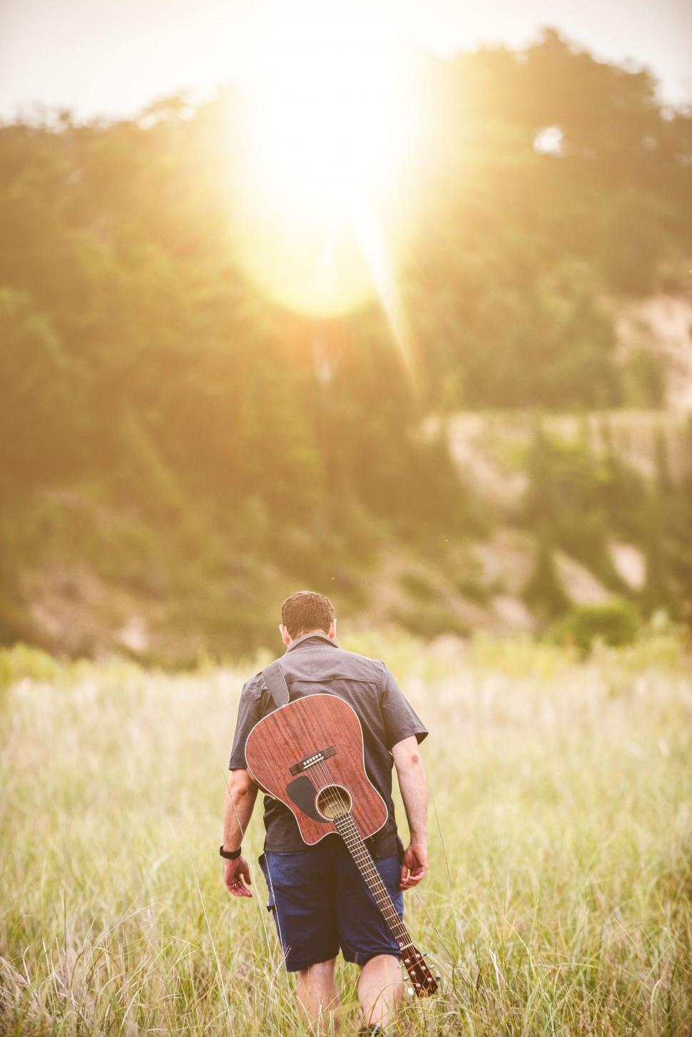 Free Image of Man Walking Through Field With Guitar 