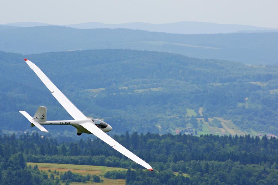 Free Image of Small Plane Flying Over Lush Green Hillside 