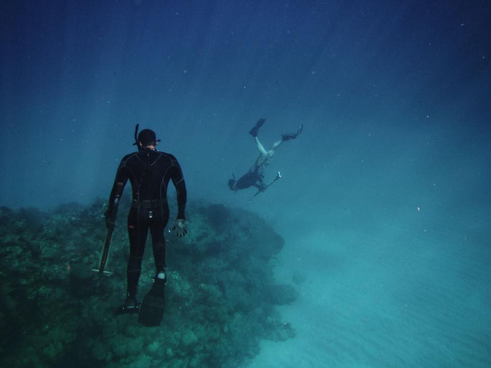 Free Image of Man in Wet Suit Standing on Top of Rock 