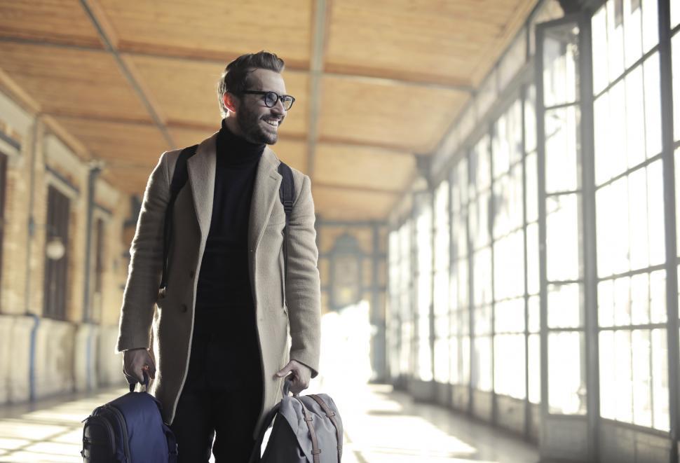 Free Image of Young Adult Man in long overcoat smiles as leaves for a journey 