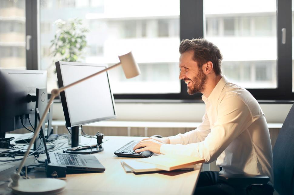 Free Image of Young Adult Man In White Shirt Smiling and Using a Computer 